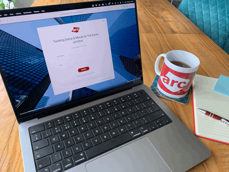 a laptop woth ARC's damp and mould webinar sign up page displaying, to the right is an ARC branded cup of coffee and a notepad with an ARC pen